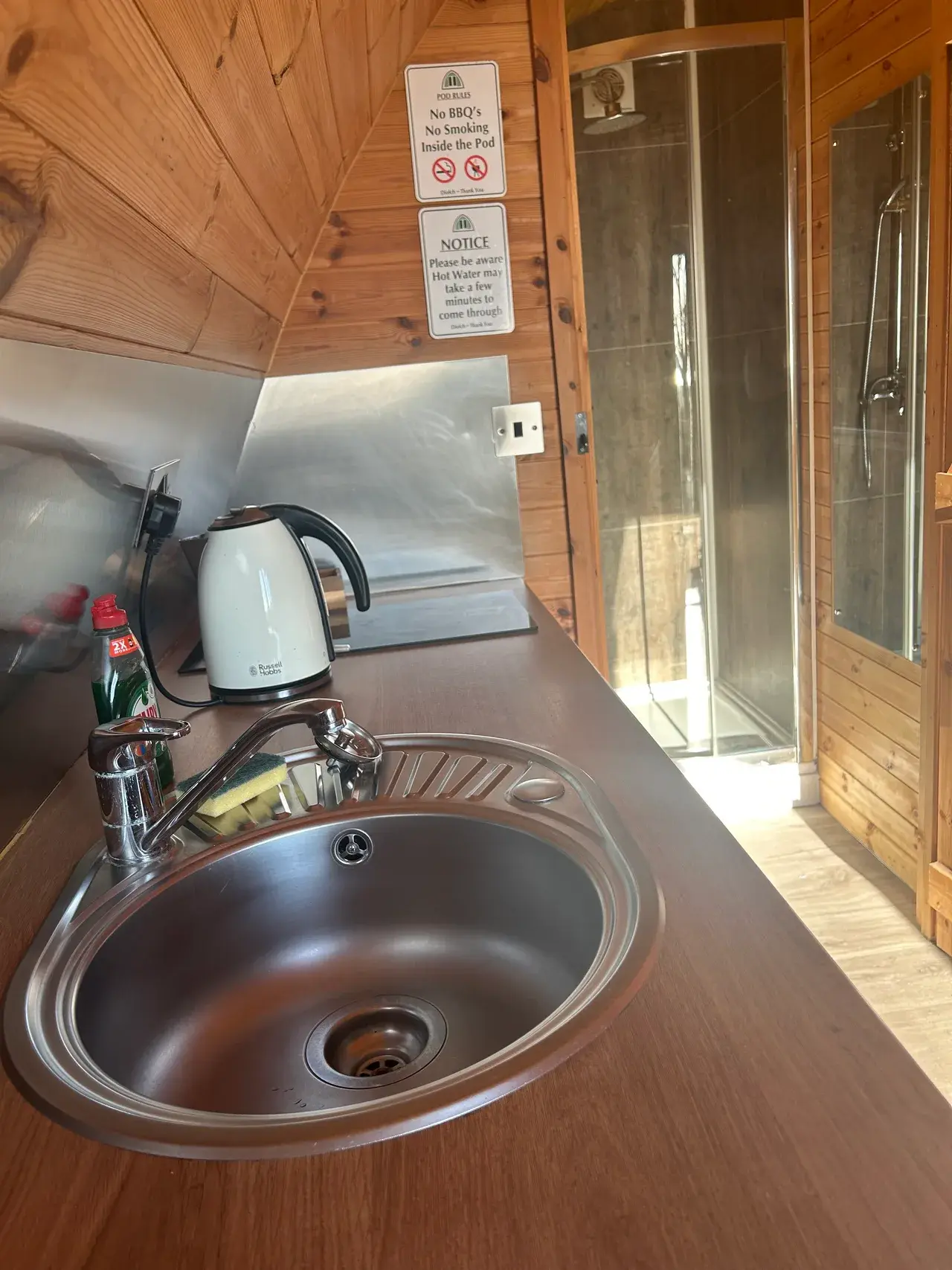 Interior of a glamping pod — fitted kitchen with kettle and sink beside the en-suite shower