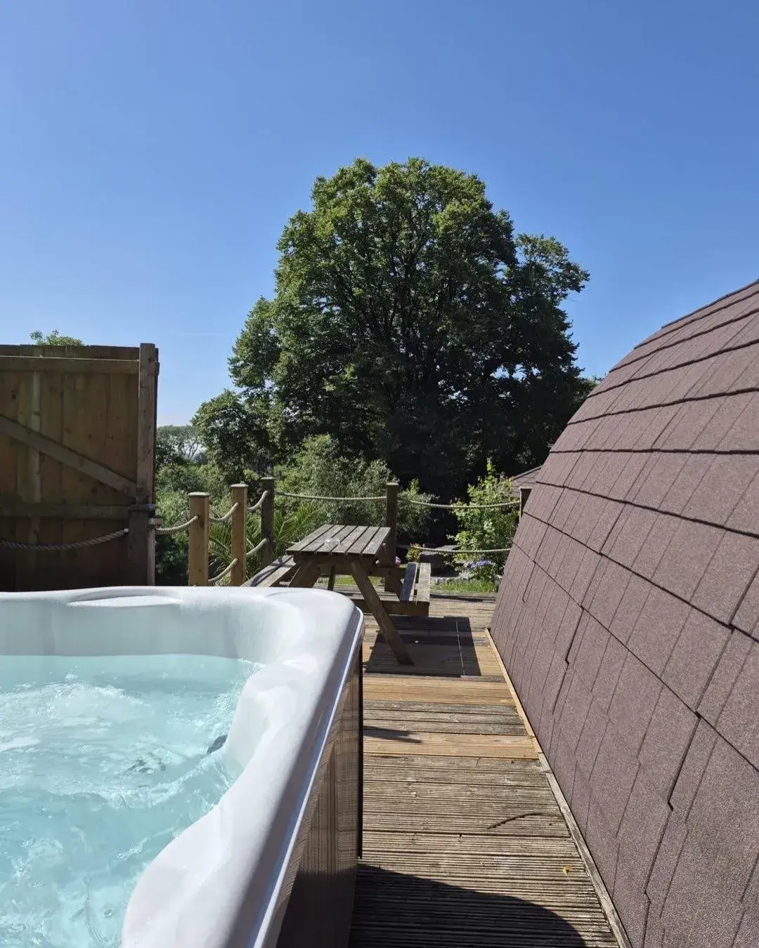 Private Jacuzzi hot tub bubbling under a clear blue sky, pod roof visible alongside